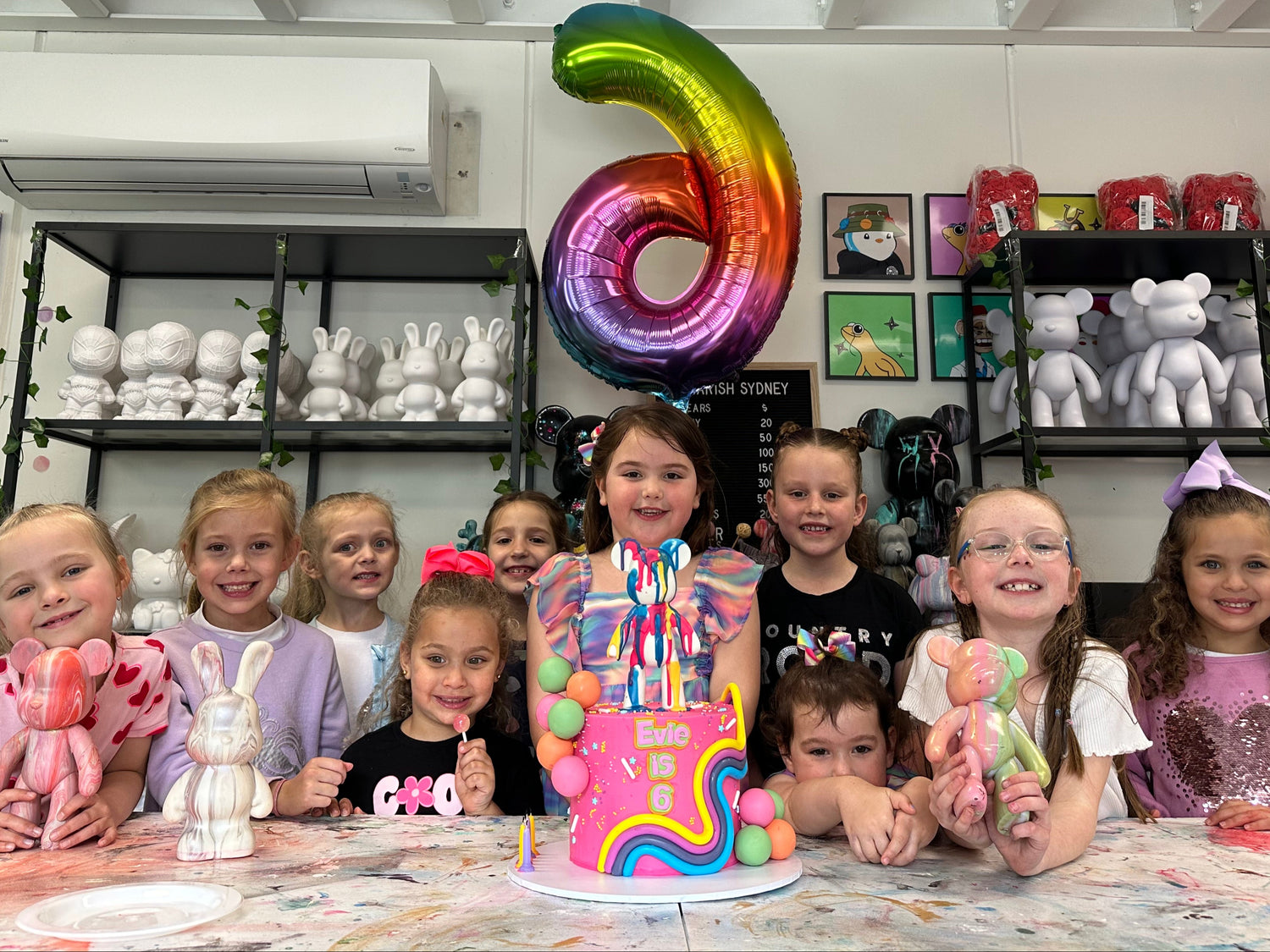 Children celebrating a birthday with a cake and balloons in a store setting.